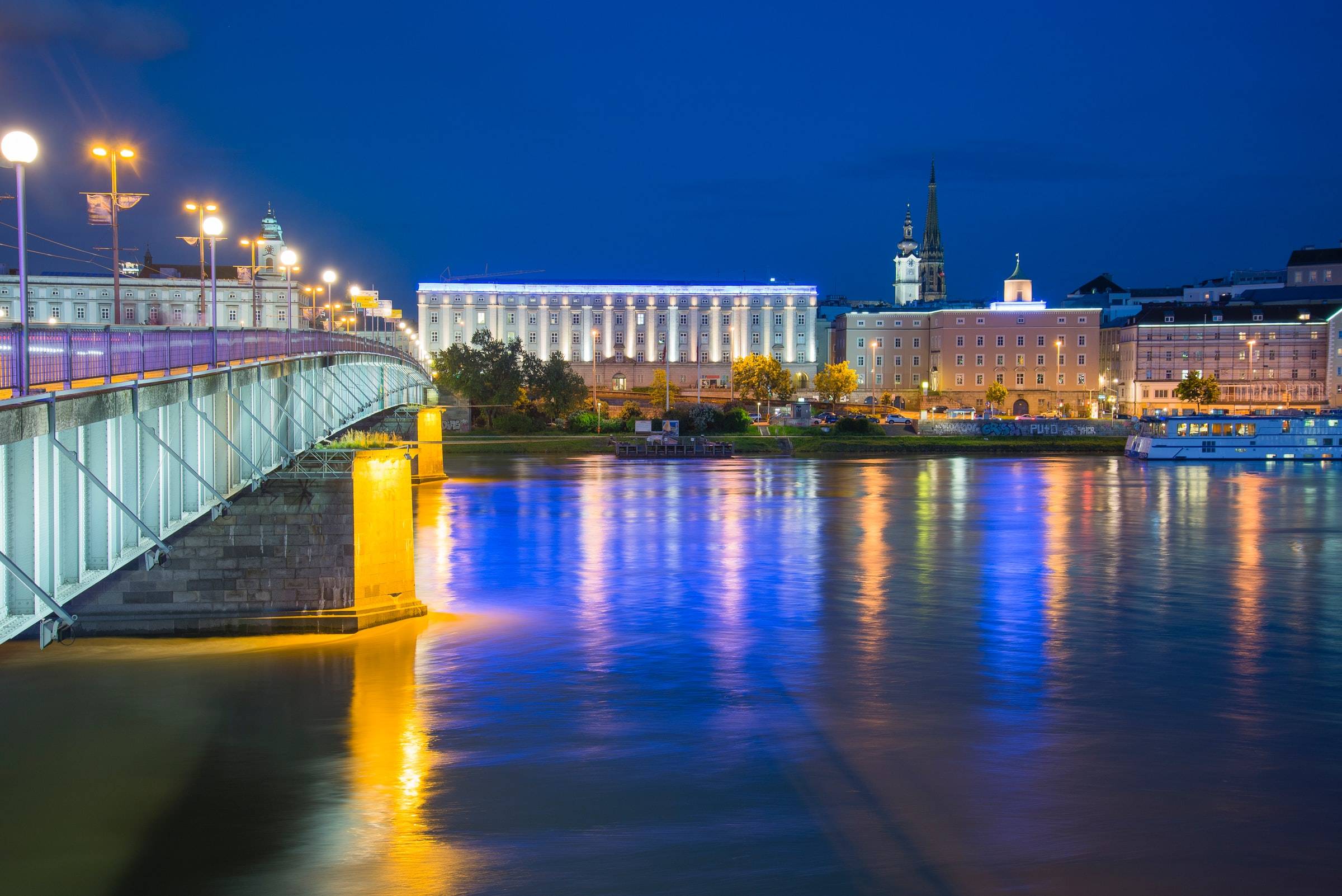 Nibelungenbrücke und Gebäude der Stadt Linz spiegeln sich bei Nacht in der Donau